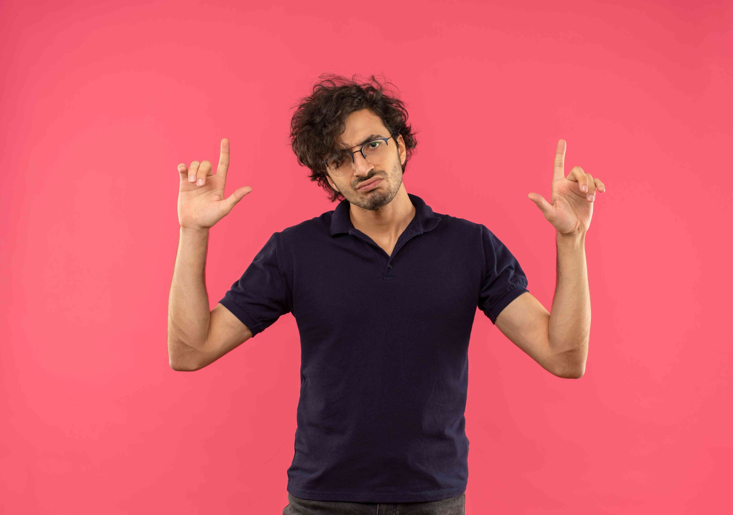 Young annoyed man black shirt with optical glasses purses his lips points up isolated pink wall 1 scaled